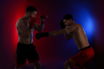 Men with boxing gloves fighting on dark background in neon lights