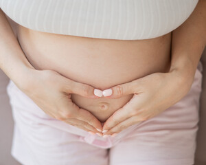 Pregnant woman holds her hands in a heart shape on her belly. 