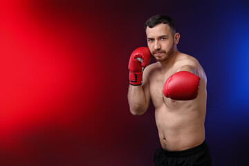 Man with boxing gloves fighting on dark background in neon lights, space for text