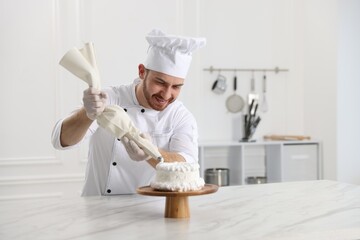 Confectioner decorating cake with cream at white marble table in kitchen, space for text