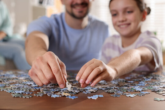 Happy father and his daughter solving puzzle together at wooden table indoors, selective focus