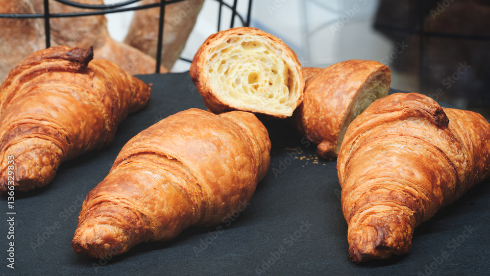 Poster close up of croissants with one of them cut open. croissants are golden brown and appear to be fresh