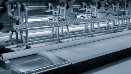 A machine is weaving a piece of fabric. The machine is made up of many parts, including a large metal piece that is connected to a hose