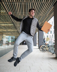 Happy businessman jumping with documents in a modern urban environment