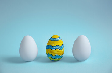A colorful Easter egg with two plain white eggs on a soft blue background. Ideal for holiday themes, festive branding, greeting cards, and seasonal marketing materials.