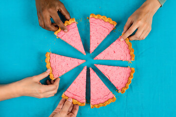 Hands taking slices of a pink pie on a turquoise background, representing sharing and community