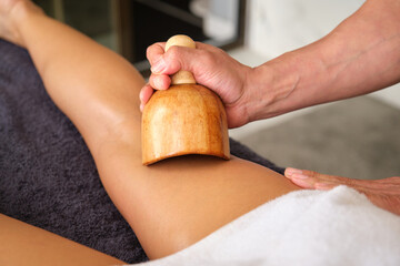 Maderoterapia anticellulite massage treatment, therapist using wooden tool massaging leg of client