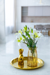 Bouquet of white artificial lilies in a golden vase on a table on a light background.