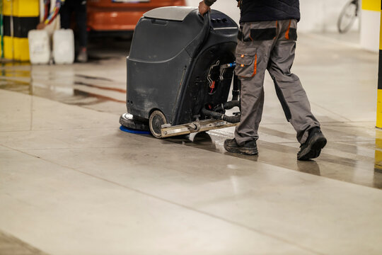 Unrecognizable worker washing garage floor with scrubber machine.