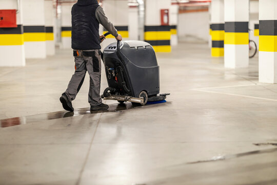 Rear view of worker using scrubber machine for cleaning garage.