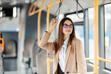 Portrait of chic lady riding city bus and holding handle while looking trough the window.