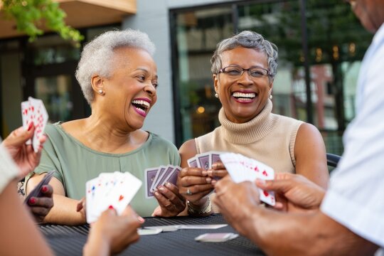 Joyful elderly african female friends playing cards outdoors