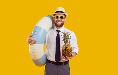 Happy office worker enjoys his summer holiday. Smiling young man in white shirt, black tie, sunglasses and sun hat holding water ring and funny pineapple isolated on yellow background