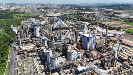 Drone sobrevoa chaminés de uma indústria de papel com denso vapor sendo liberado. Destaque para...