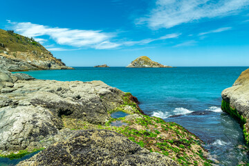 Part of Praia Grande, with many mountains and rocks covered in moss, crystal clear sea and a small island in the background. Near the city of Cabo Frio, Rio de Janeiro, Brazil.