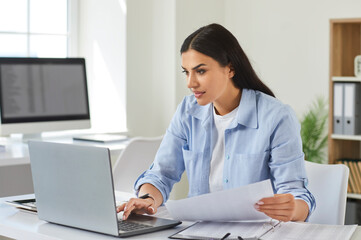Young beautiful brunette woman accountant in causal shirt sitting at office desk, doing business...
