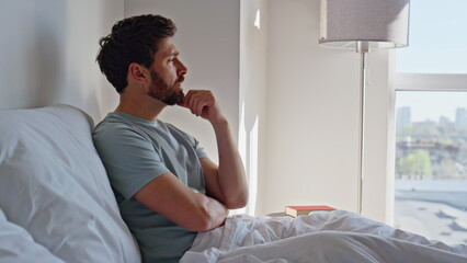 Sad guy sitting bed modern hotel room feeling unhappy closeup. Upset man morning