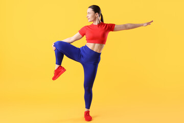 Woman in sportswear exercising on orange background