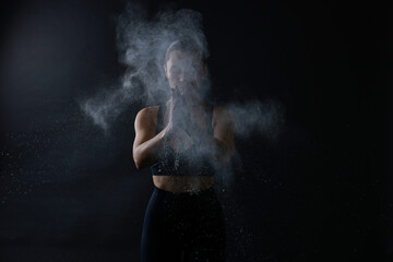 Woman clapping hands with talcum powder before training on black background