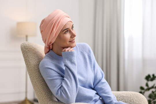 Smiling woman with cancer in headscarf on armchair indoors
