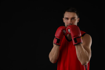 Man in boxing gloves on black background, space for text