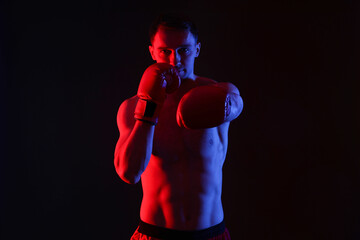 Man in boxing gloves fighting on black background in neon lights