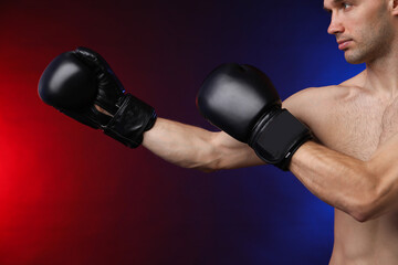 Man with boxing gloves fighting on dark background in neon lights, closeup