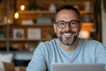 Fototapeta premium A smiling man in a gray sweater shows confidence while working on a laptop in a stylish, modern workspace filled with wooden shelves and soft lighting.