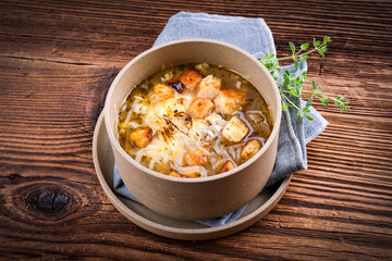 Traditional French onion soup with onion rings, pieces of bread and grated mountain cheese served as a close-up in vegetable broth in a designer plate on a rustic wooden table