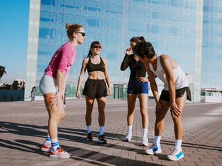 A multinational group of young people outdoors in athletic gear, laughing and chatting after a...