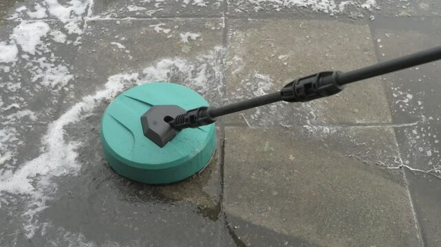 round high-pressure washer spraying foaming water on cement tiles overgrown with grass and dirt