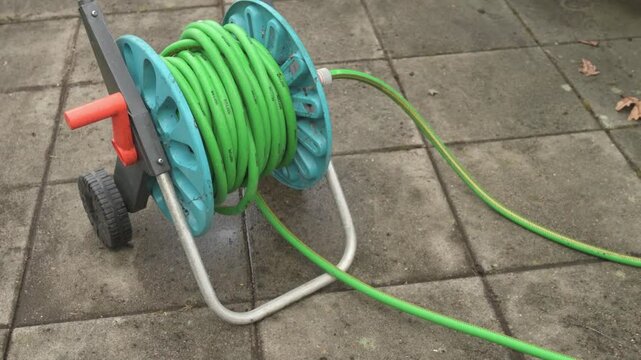 a hose reel with a green hose standing on freshly washed cement slabs