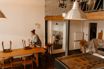 Female owner standing and removing chairs from table in front of her, preparing for cafe opening