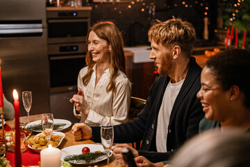 Family and guests sitting at the table and laughing during dinner, in the living room, during Christmas