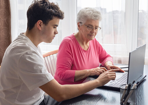 Grandson helping grandmother with computer, teaching digital skills, elderly woman learning technology, family support, intergenerational communication, senior education, online learning assistance. 