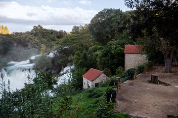 Lush vegetation surrounds old watermills near the majestic waterfalls of Krka national park in Croatia, creating a picturesque scene of nature and history blending together