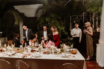 Bride and groom sitting at a table and talking to a group of three guests standing next to them, in a restaurant, at a wedding
