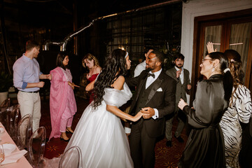 A bride and groom dance and smile while a group of seven guests dance around them at a wedding party