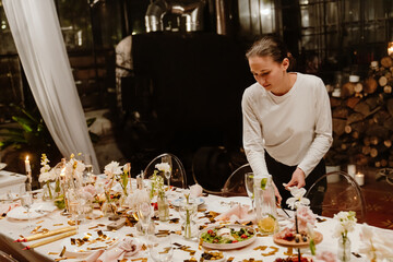 A female waiter stands and clears dishes from the table, in an establishment, after a wedding celebration