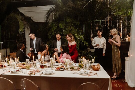Bride and groom sitting at a table and talking to a group of three guests standing next to them, in a restaurant, at a wedding