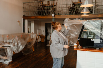 The woman owner stands and removes a bag from the equipment before opening the cafe