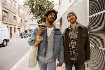 Gay couple, man walking and holding the hand of man walking next to him and pointing up, on the...