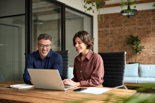 Female manager showing financial results to colleague at work. Two professional team business man and woman using laptop at corporate meeting. Happy busy executive people working together in office. - Powered by Adobe