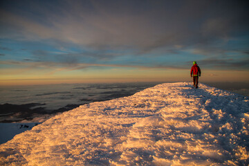 A person on the summit of Mount Rainier above 14,000 feet at sunset in Washington State over the...