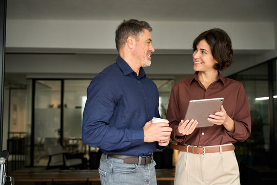 Two happy hispanic professional business man and woman having friendly conversation at work. Executives team business people working talking at workplace discussing project plan in corporate office.