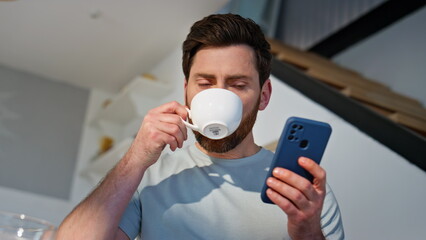 Morning guy reading cellphone message drinking coffee at home cuisine closeup