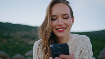 Carefree girl browsing cellphone social media sitting windy nature alone closeup