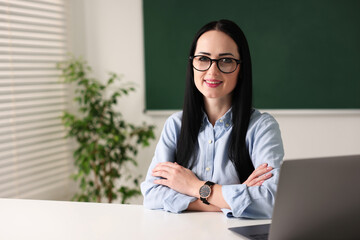 English teacher with laptop at desk in classroom. Space for text