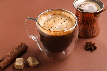 Glass cup and jezve of hot espresso on brown background