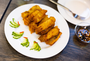 Asian restaurant serves platter of appetizers. Pieces of eel fillet, fried to crispy crust, garnished with cucumber slices.